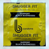 A yellow condom wrapper displaying the "bCondoms" logo and labeled with "b Condoms Snugger Fit (49mm)" includes text promoting the message "SUPPORT BLACK BUSINESSES" and features the website www.bcondoms.com. Crafted from ultra-smooth natural rubber latex, it guarantees quality assurance. The backdrop is artistically blurred with light bokeh effects.